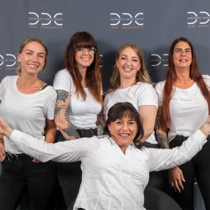 Teamfoto des Domaniecki Dental Centers mit fünf Zahnärztinnen und zahnmedizinischen Fachangestellten in weißen Shirts vor einem grauen Hintergrund. Die Gruppe strahlt Freundlichkeit und Professionalität aus